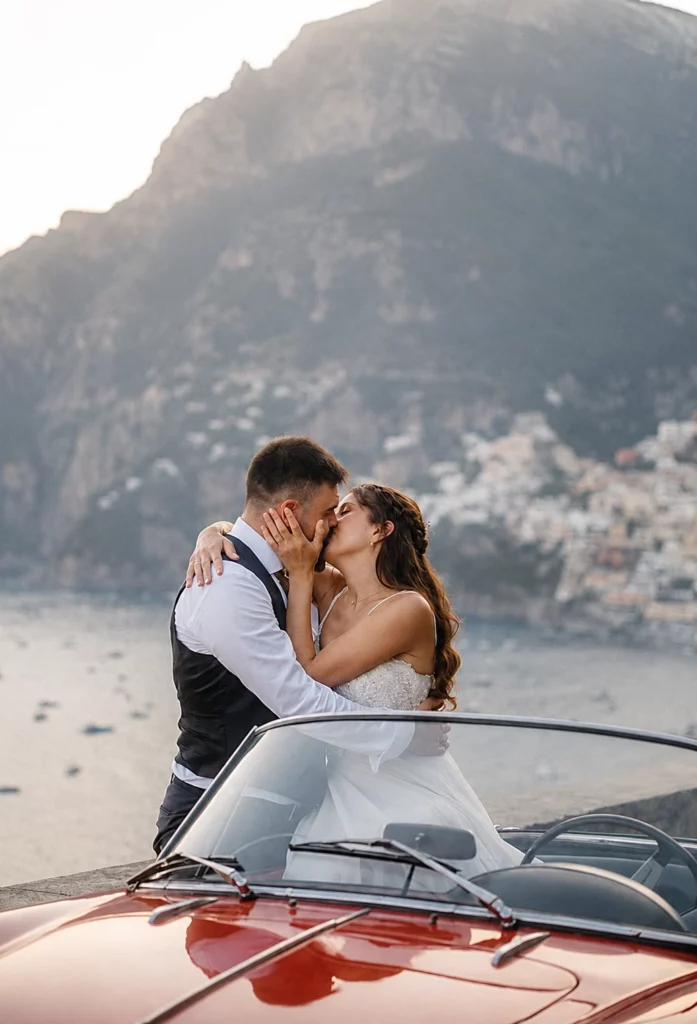 Bride and groom kissing beside a vintage red classic car during an Amalfi Coast elopement in Italy