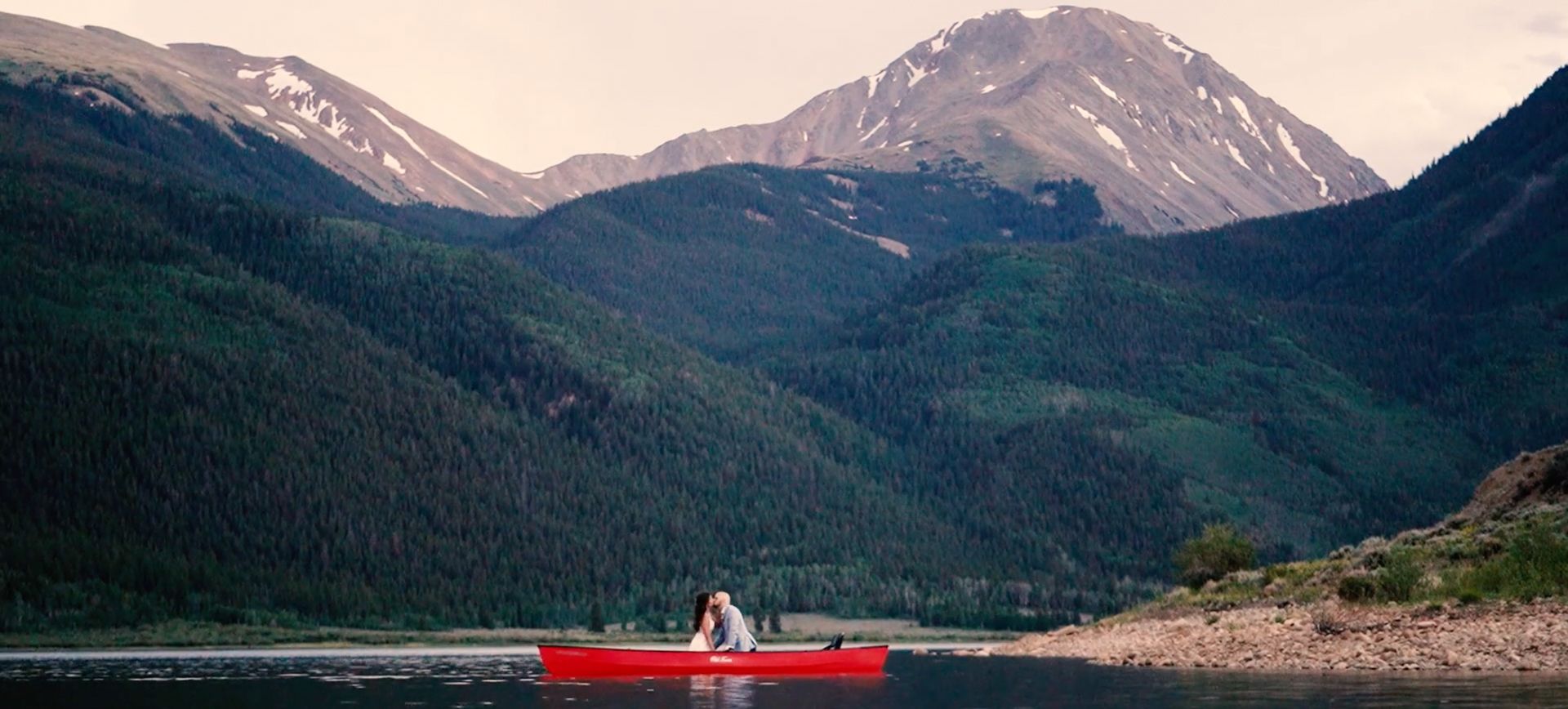Eloping couple kissing in a red canoue in a lake